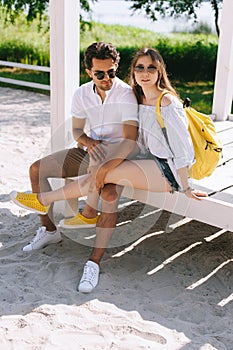 heterosexual couple sitting on wooden bench at sandy