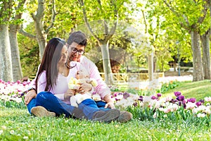 Heterosexual Latino couple sitting in a park with their newborn baby