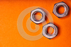 Hex nuts on orange background. Bolted connection elements