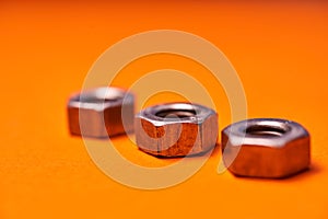 Hex nuts on orange background. Bolted connection elements