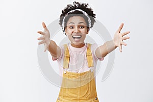Hey come here and hug me. Indoor shot of charming caring friendly-looking dark-skinned woman in headband and overalls