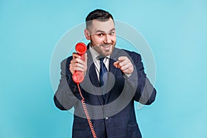 Hey you, call me. Bearded young adult male wearing dark official style suit, holding retro phone