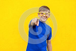 Hey you!Happiness freckled boy in yellow glasses, pointing finger and looking at camera.