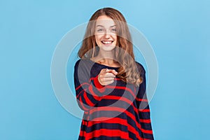 Hey you. Happy woman wearing striped casual style sweater pointing to camera and looking with