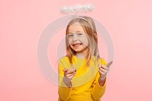 Hey you lucky! Happy cute positive little girl with angelic halo pointing fingers to camera and looking at camera