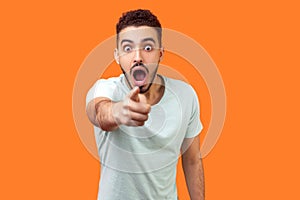 Hey you! Portrait of amazed brunette man pointing finger at camera. isolated on orange background