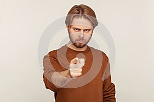 Hey you! Portrait of angry bossy strict man with beard wearing sweatshirt pointing finger, indicating direction