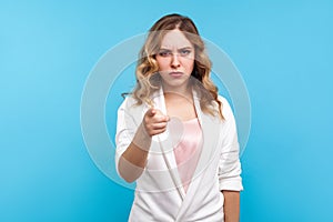 Hey you! Portrait of angry woman pointing finger at camera with serious gloomy face. blue background