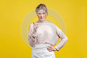 Hey you! Portrait of angry young woman with blonde hair in casual beige blouse,  on yellow background