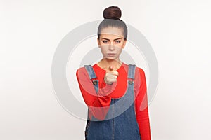 Hey you! Portrait of bossy dissatisfied angry girl with hair bun in denim overalls pointing finger to camera, blaming photo