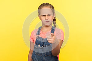 Hey you! Portrait of bossy little girl in denim overalls pointing to camera and looking with angry displeased expression