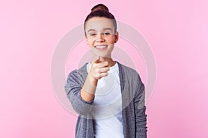 Hey you! Portrait of cheerful brunette teenage girl pointing at camera and smiling genuinely. studio shot isolated on pink