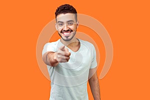 Hey you! Portrait of cheerful handsome brunette man pointing finger at camera. isolated on orange background