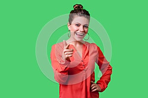 Hey you! Portrait of lovely positive young woman with bun hairstyle, big earrings and in red blouse. isolated on green background