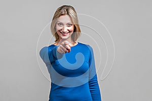 Hey you! Portrait of positive elegant woman pointing at camera and smiling. isolated on gray background