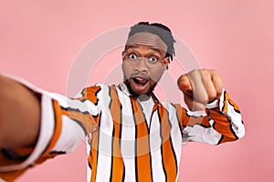 Hey you! Surprised african man blogger with beard and dreadlocks in stylish eyeglasses and striped shirt pointing finger at you