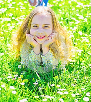 Heyday concept. Girl on smiling face spend leisure outdoors. Girl lying on grass at grassplot, green background. Child photo