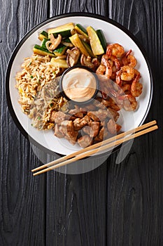 Hibachi dish consisting of fried rice with egg, shrimp, steak and vegetables served with sauce closeup in a plate. Vertical top