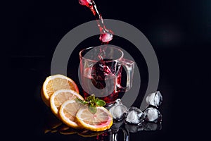 Hibiscus cold tea pouring into glass with ice, lemon and mint isolated on black background