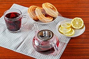 Hibiscus tea in a cup next to a teapot and sweets on a salad table on the table.