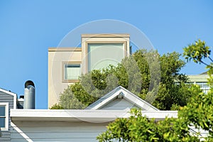 Hidden house tower with bright trees and smaller rooftops in midday sun with clear blue sky background.