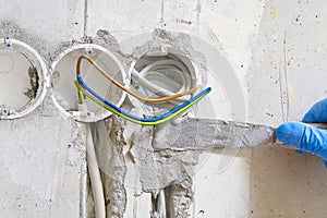 Hidden installation of electrical wires for sockets to a concrete wall. The master is plastering the strobes with the