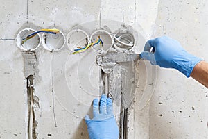 Hidden installation of electrical wires for sockets to a concrete wall. The master is plastering the strobes with the