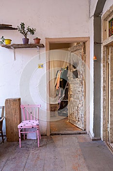 Hidden second-hand clothing store with pink chairs, plants, shelves, a wardrobe, and white walls.