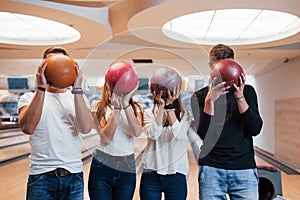 Hiding faces behin the balls. Young cheerful friends have fun in bowling club at their weekends