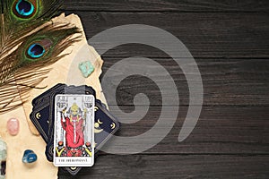 The Hierophant with other tarot cards near peacock feathers and gemstones on black wooden table, flat lay. Space for text