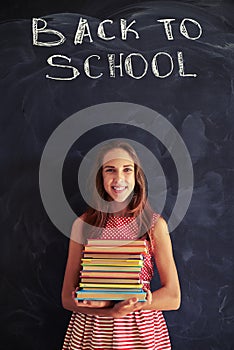 High achiever schoolgirl standing with books against blackboard