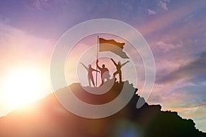 High achiever, silhouettes of three people holding on top of a mountain to raise their hands up.