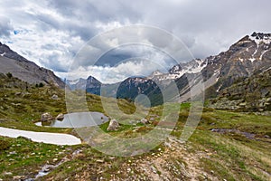 High altitude alpine pond in extrem terrain rocky landscape once covered by glaciers. Dramatic stormy sky and snowcapped mountain