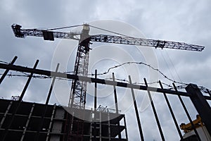 High altitude construction crane over an concrete frame of high-rise building behind a barbed wire fence