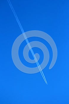 High altitude flying passenger plane over clear blue sky leaving two dense white trails