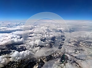 High altitude photograph of the snow covered alps with blue sky and white clouds covering the earth with curved horizon