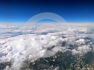 High altitude view of the earth from an airplane with deep blue sky and clouds covering a mountain landscape