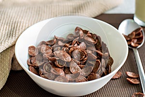 High angel view of chocolate cereal in a white bowl on brown background