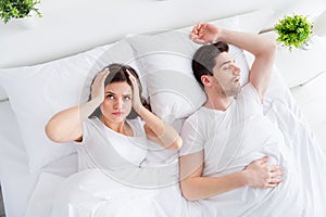 High angle above view photo of pretty lady covering ears handsome snoring husband guy couple lying sheets bed covered