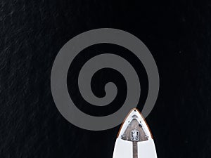 High angle aerial bird`s eye partial view of the bow of a long white luxury yacht with wooden deck in dark blue waters