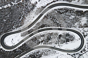 High angle aerial view drone image on the curved serpentine road trough the trees and forest in mountain range with white snow in