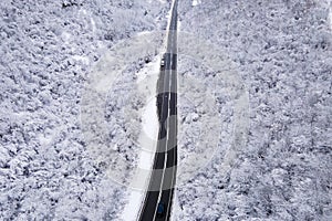 High angle aerial view drone image on the road trough the trees and forest in mountain range covered with white snow in winter day