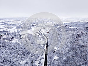 High angle aerial view drone image on the road trough the trees and forest in mountain range covered with white snow in winter day