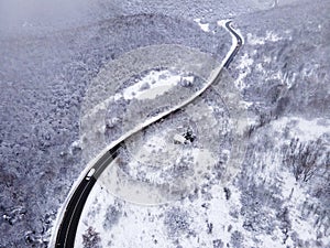 High angle aerial view drone image on the road trough the trees and forest in mountain range covered with white snow in winter day