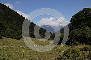 High-angle of Aran valley, forested, misty, sunlit Pyrenees mountain range, cloudy sky background