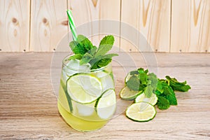 High angle close up of ice cold  cocktail of gin and tonic soda garnished by lemon slice and mint leaves on wooden background.