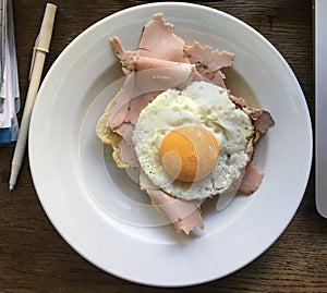 High angle close up over a plate with a sunny side up egg abd ham next to a pen