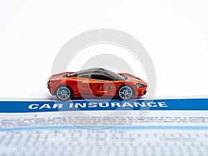 High angle close up shot of an orange sports car toy with insurance paper on white background