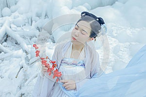 High-angle closeup of a Chinese girl with bright clothes holding red flowers snowy background