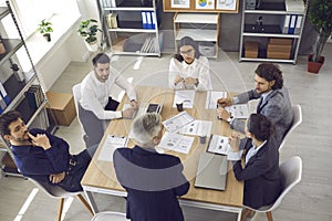 Team of young workers listening to senior manager sitting around office table in corporate meeting